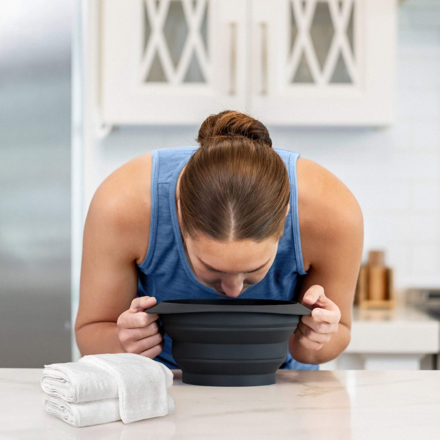Woman performing an ice facial plunge using Icy-Mojo face ice bath bowl on kitchen counter.